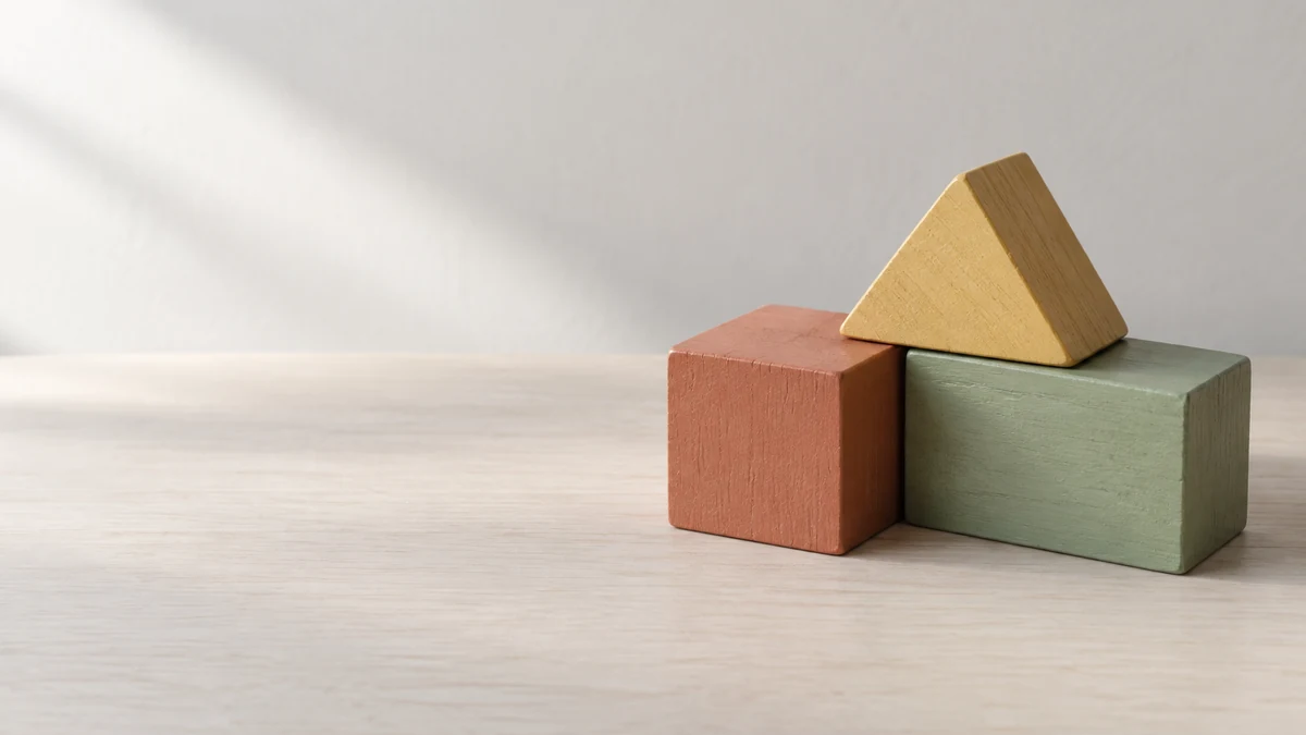 Drei verschiedenfarbige Holzbausteine stehen rechts auf einer neutralen Fläche, links bleibt Raum für eine Überschrift.